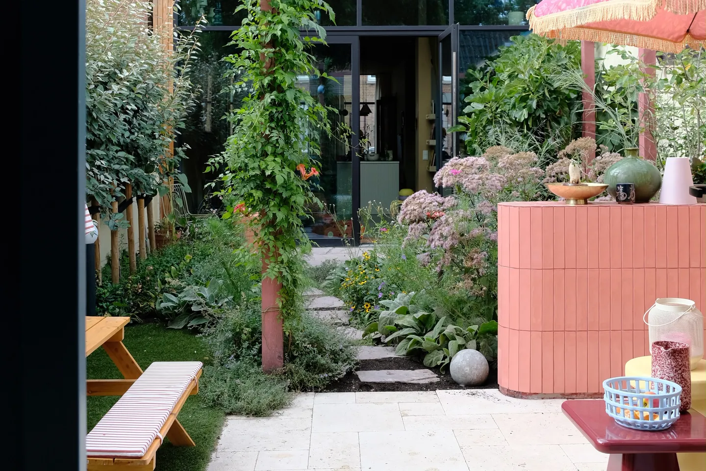 De gerealiseerde tuin in bloei, met natuurstenen pad, borders en de betegelde buitenbar