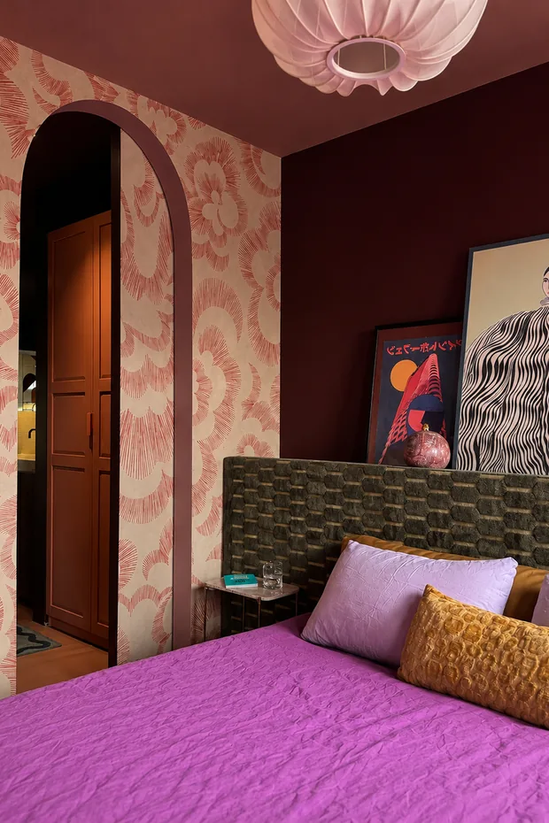 Slaapkamer met zelf behangen bloemenbehang, een gemetselde boogdoorgang met doorkijk naar de en-suite met deuren op maat, en een gestoffeerd hoofdeind op maat